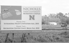 A sign displayed by the site of the future recreation complex shows an aerial view of what the complex will look like, as well as the schedule of construction, while construction work continues on intramural fields.