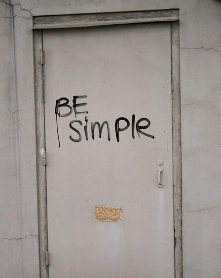Graffitied words “Be Simple” on a door in Downtown Thibodaux. The words almost look like it was fingure painted and are repeated in several different places in downtown.