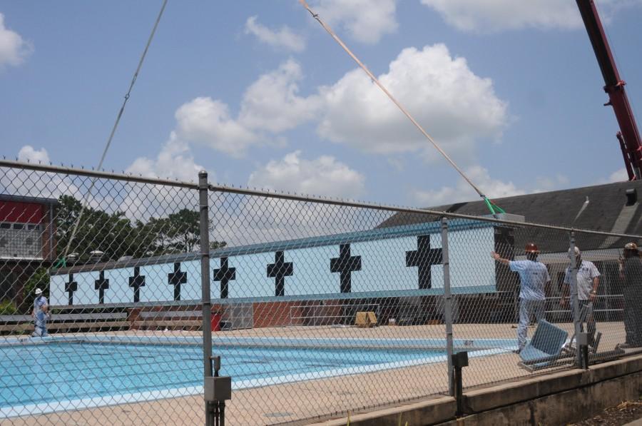 A crane operator and ground workers lift a movable bulkhead over the Crawfish Aquatics building and place it into J. J. Ayo Pool on June 12. This bulkhead will allow the pool to change from one 50 meter pool to two 25 meter pools to use for competitions.